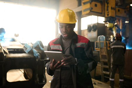 African American engineer or foeman scrolling in tablet while standing in front of camera in...