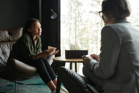 Young stressed African American woman explaining her problem to female counselor sitting in front of her during psychological sessionの写真素材