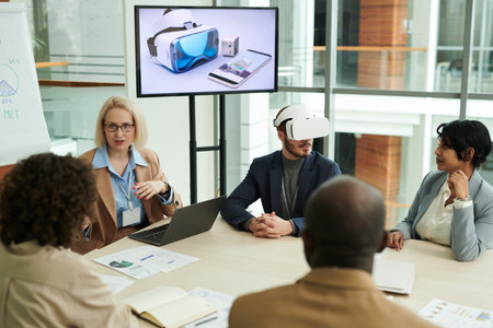 Group of intercultural colleagues discussing points of presentation being made by mature blond female speaker sitting among employeesの写真素材