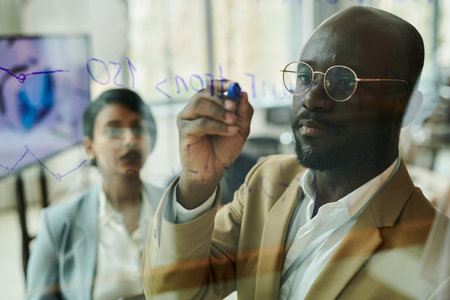 Focus on young serious African American businessman or coach with blue highlighter writing on...