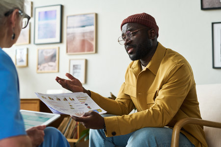 Confident African American male economist explaining financial charts to female colleague while sitting in front of her during discussionの写真素材