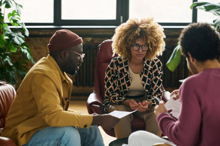 Young serious African American businesswoman looking at one of male colleagues during discussion of financial data at working meetingの写真素材