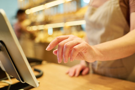 Selective focus on hand of mature female clerk entering prices of products in computer database while standing by counter desk in front of tabletの写真素材