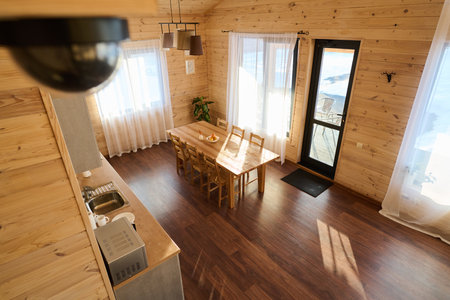Spacious cozy kitchen with wooden table and chairs, curtains on windows, counter with microwave oven, kitchenware and metallic sinkの写真素材