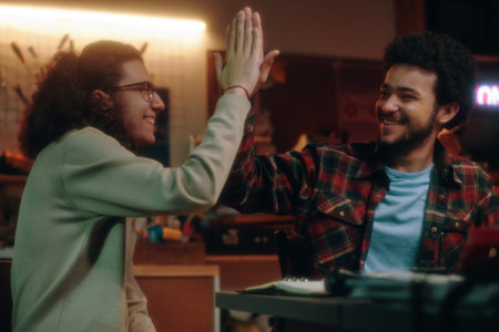 Young guys giving high-five to each other while working in workshop, they creating successful...