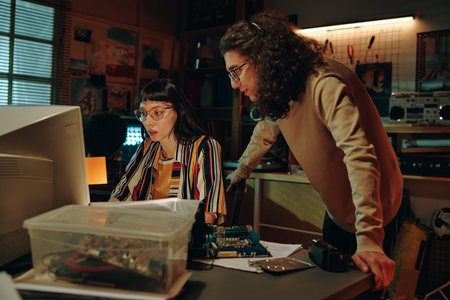 Young people discussing development of software on computer during their teamwork in garage