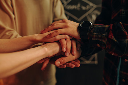 Close-up of team of young people holding hands and supporting each other during their business projectの写真素材