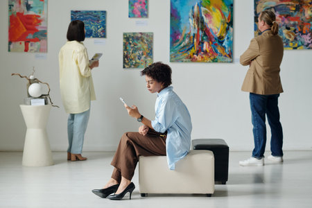 Woman resting on couch and using smartphone during her visit to art galleryの写真素材