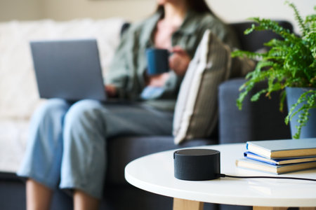 Close-up of smart speaker standing on table and using to listen to music and news with woman working...