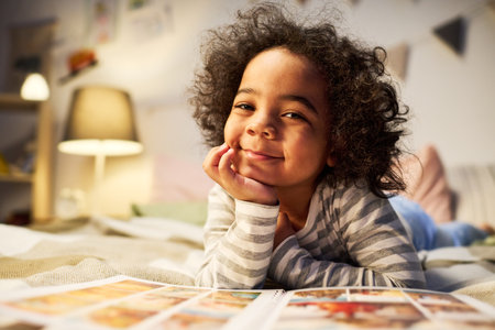 Portrait of African American little boy smiling at camera while lying on bed with fairytale book