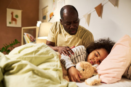 Little son sleeping in his bed with toy while dad putting him and telling tale to himの写真素材