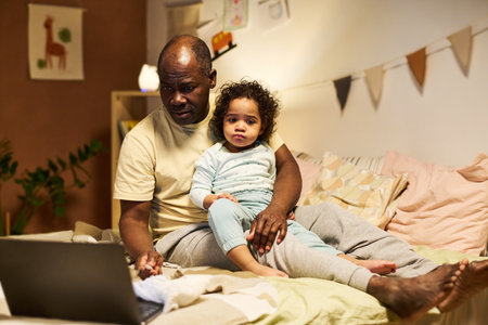 African American dad working online on laptop while sitting with baby at homeの写真素材