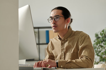 Young Asian male entrepreneur looking at online financial data on computer screen while analyzing it...
