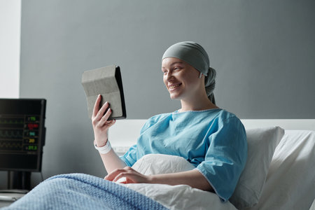 Young smiling woman with oncological illness looking at tablet screen while communicating with her...