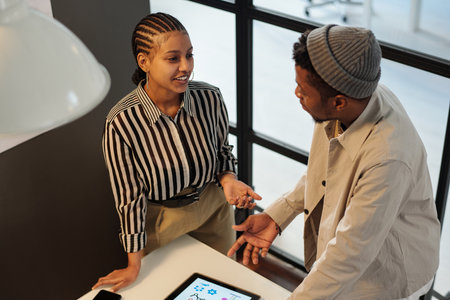 Two young confident African American architecture designers having discussion of new ideas and plans while standing by workplaceの写真素材