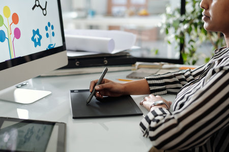 Hand of young African American graphic designer with stylus and touchpad drawing sketches while...