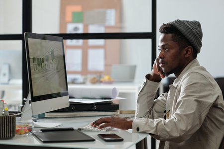 Young serious male architect or designer looking at graphic sketches on computer screen while...