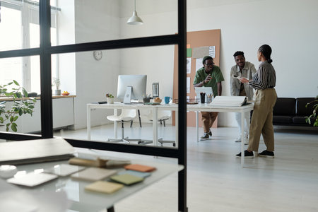 Long shot of young African American designers in casualwear talking at meeting and discussing new creative ideas while standing by workplaceの写真素材