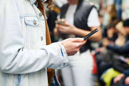 Close-up of young man in denim jacket texting in mobile phone or watching video while standing in...