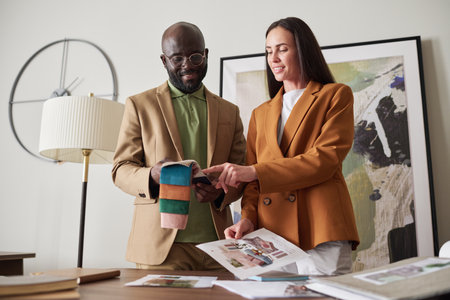 Two young creative designers choosing color and textile from sample collection while working over...