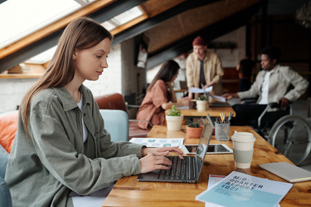 Side view of young serious female accountant or broker typing on laptop keyboard and looking at screen with online information in officeの写真素材