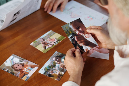 Focus on hands of grandfather holding picture of his cute granddaughter over wooden table with set of photos of other grandchildrenの写真素材