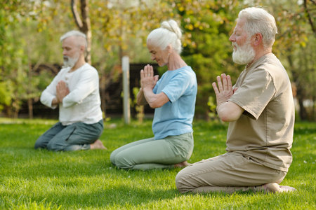 Focus on bearded senior man keeping hands put together by chest while practicing yoga exercise with other patients of retirement homeの写真素材