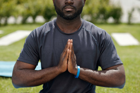 Cropped shot of young African American man in t-shirt keeping palms put together by chest while...