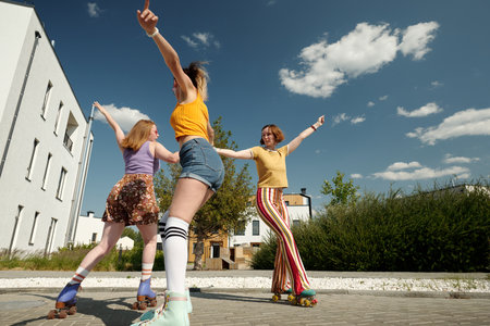 Three happy girls whirling on roller skates in front of camera and having fun while enjoying leisure...