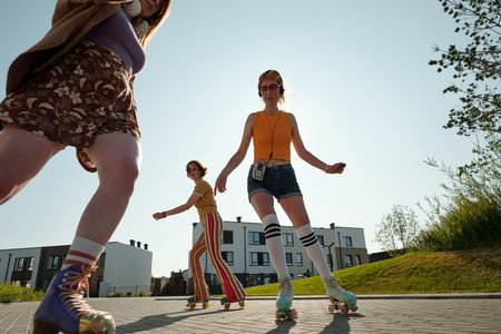 Long shot of three young active girlfriends on roller skates moving in front of camera along street...