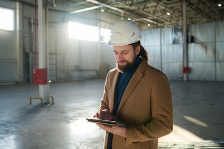 Young confident contractor or owner of warehouse scrolling in tablet through online information or...
