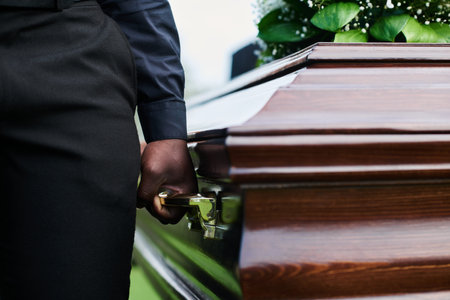 Close-up of man holding wooden coffin by one of several handles while carrying it with other people after farewell ceremony at funeralの写真素材