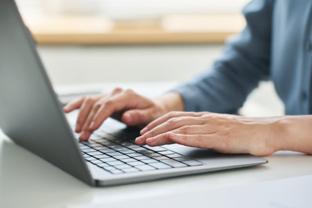 Close-up of young female employee or chief executive officer with laptop entering data or...