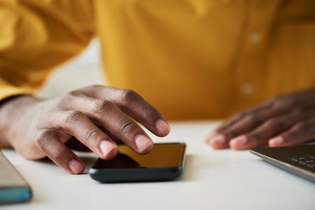Focus on fingers of right hand of young male office worker over smartphone screen scrolling through contacts while sitting by deskの写真素材