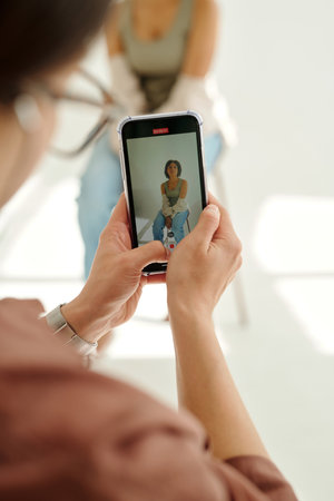 Focus on smartphone screen with shot of young female fashion model in hands of photographer taking...