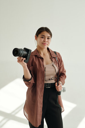 Young creative brunette woman with two professional photocameras standing in isolation while waiting...