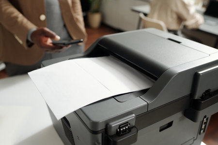 Plastic grey xerox machine with paper document on tray standing on workplace of office manager or...