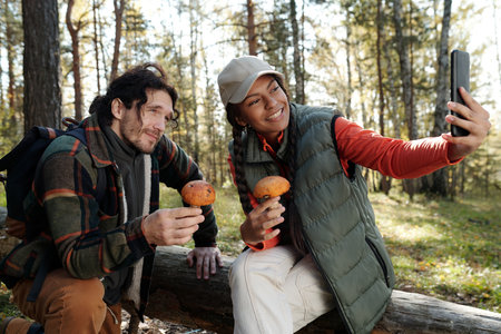 Happy young woman with smartphone and orange cap boletus mushroom taking selfie with her husband...