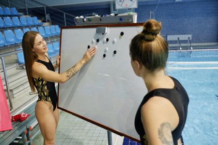 Young confident female water polo trainer operating with small black and white magnets on blank...
