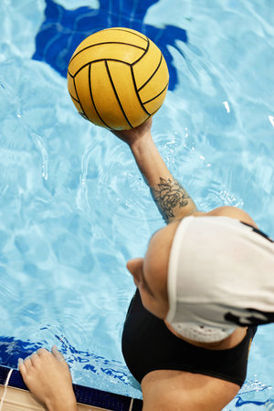 Top view of young female athlete in swimwear holding yellow ball while standing in swimming pool with pure blue water during gameの写真素材