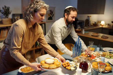 Mature woman putting plates with homemade donuts and humus on table being served for guests before celebration of Hanukkahの写真素材