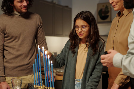 Pretty pre-teen girl lighting blue candles of menorah while standing among her family and preparing for Hanukkah celebrationの写真素材