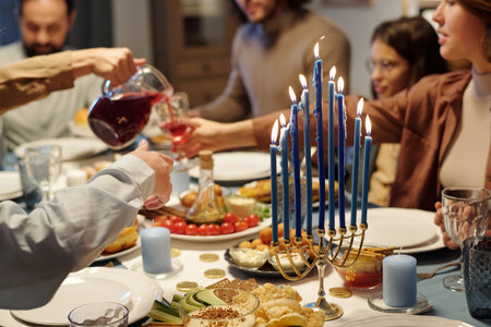 Focus on blue burning candles on menorah candlestick standing on table served with homemade food and drinks during Hanukkah family dinnerの写真素材