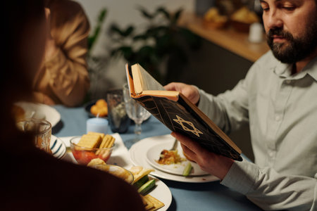 Close-up of mature Jewish man holding open Old Testament over served table and reading Psalms to his family members during dinnerの写真素材