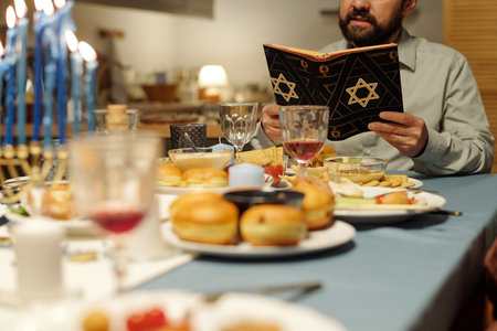 Focus on cropped mature man reading Torah in black cover with star of David while sitting by festive table served with homemade foodの写真素材