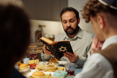 Focus on bearded rabbi and head of Jewish family reading text from Torah while sitting by served table in front of his two childrenの写真素材