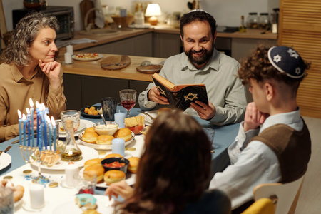 Happy bearded man with open Scripture sitting in front of his family and looking at daughter during discussion of text from Old Testamentの写真素材