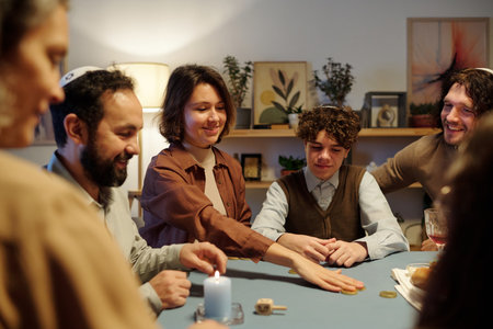 Young smiling woman putting coin on center of table while betting during leisure game with members of her family after Hanukkah dinnerの写真素材