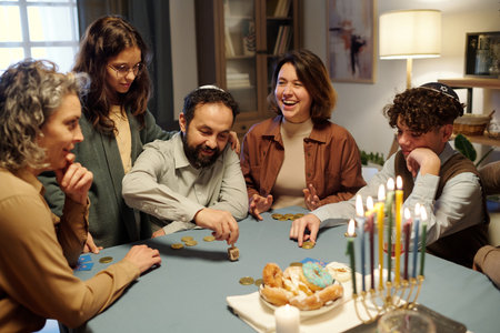 Young cheerful woman laughing while sitting next to mature man spinning small dreidel during leisure game among family membersの写真素材