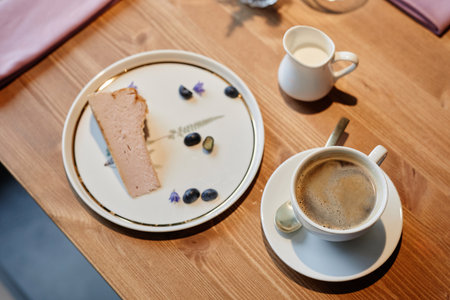 Above angle of wooden table in restaurant or cafe with cup of aromatic cappuccino and plate with piece of fresh tasty cheesecakeの写真素材